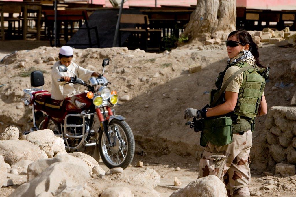 Female soldier in sunglasses in front of an afghan boy on a red motorcycle.